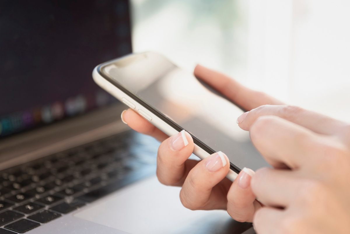 mujer sostiene teléfono con la computadora en el fondo