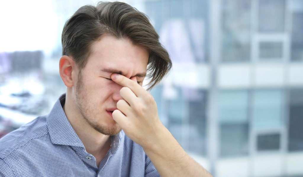 hombre se frota ojos en ciudad